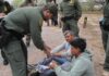 law enforcement officer handcuffing two seated men outdoors