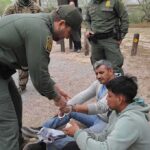 law enforcement officer handcuffing two seated men outdoors