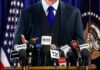 Musk Drag Triggers DOJ Cloud Over Newsom A speaker at a press conference with multiple microphones in front of them