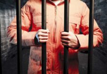 Judge Sparks Fury After Triple-Fatal Crash Person in an orange jumpsuit gripping prison bars in a dark cell