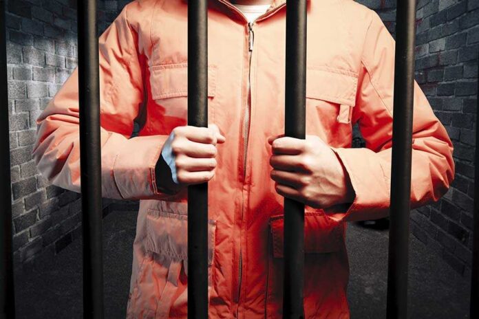 Dark,Prison,Cell,At,Night Person in an orange jumpsuit gripping prison bars in a dark cell