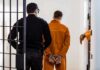 Army Child Abuse Case Shocks Fort Bragg Prisoner in orange jumpsuit handcuffed and escorted by officer