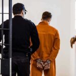 Army Child Abuse Case Shocks Fort Bragg Prisoner in orange jumpsuit handcuffed and escorted by officer