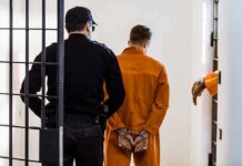 Army Child Abuse Case Shocks Fort Bragg Prisoner in orange jumpsuit handcuffed and escorted by officer