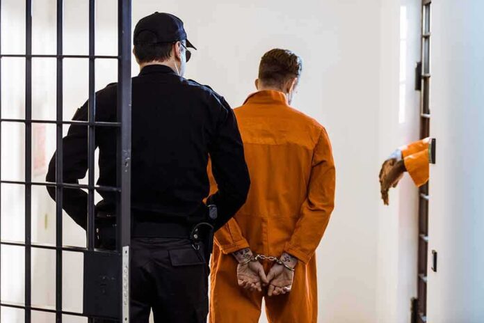 shutterstock_1030254064 Prisoner in orange jumpsuit handcuffed and escorted by officer