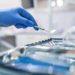 Gloved hand holding a dental mirror over instrument tray