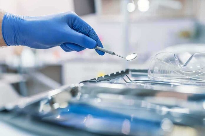 shutterstock_1163522302 Gloved hand holding a dental mirror over instrument tray