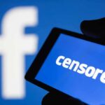 smartphone screen showing the word censored against a blue social media logo backdrop