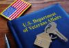 VA folder with house keychain and US flag patch on wooden desk