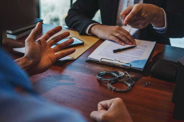 Two people discuss documents at a desk with handcuffs in view