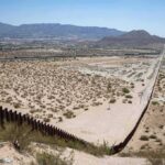 Border fence cutting across a desert landscape with mountains in the distance