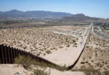 Border fence cutting across a desert landscape with mountains in the distance