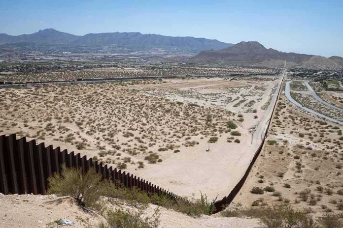 Border fence cutting across a desert landscape with mountains in the distance