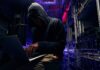 Hooded person using a laptop in a dark server room