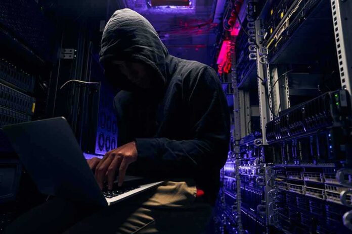shutterstock_2067215408 Hooded person using a laptop in a dark server room