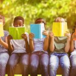 Children sitting on a bench reading colorful books outdoors