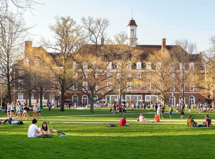 shutterstock_1037739901 Students relaxing on a campus quad in front of a brick academic building