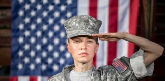 soldier in camouflage uniform saluting in front of a U.S. flag