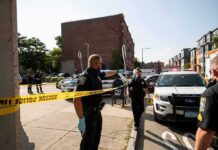 Police officers secure an urban street with yellow tape near patrol cars