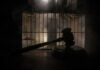 Judge’s gavel in silhouette before prison bars