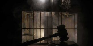 Judge’s gavel in silhouette before prison bars