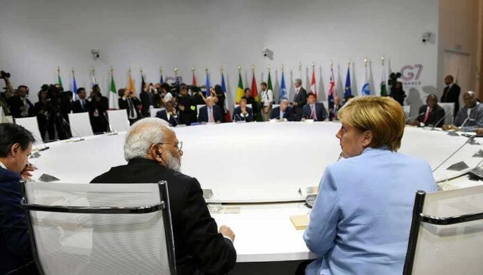 shutterstock_1970862773 Angela Merkel and Narendra Modi seated at a large round table during an international summit