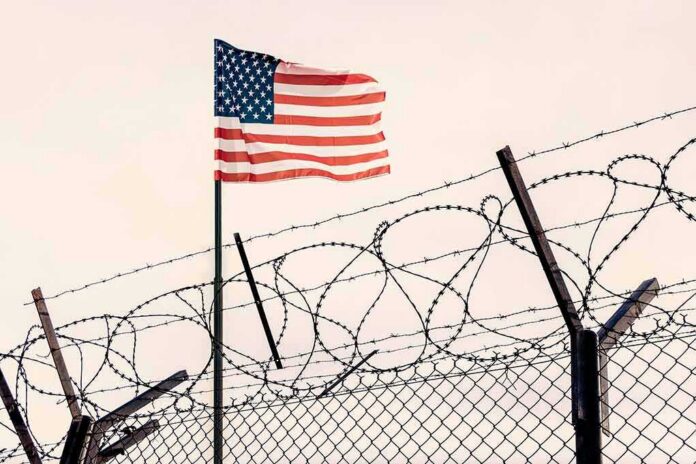 shutterstock_2165855107 American flag above barbed wire fence