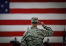 Quiet Update, Big Shock: 19th Fallen Listed Soldier saluting before a large American flag