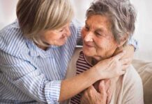 Two older women share a warm embrace on a couch