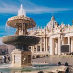 Stone fountain in front of a grand basilica with dome and colonnade