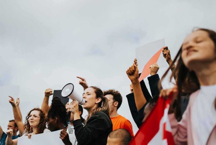 Protesters raise fists and signs as a woman speaks into a megaphone