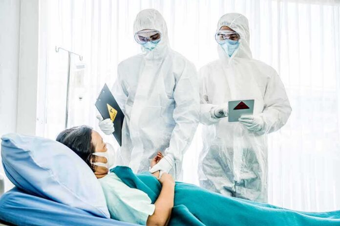Medical staff in hazmat suits attend to a patient in a hospital bed
