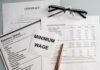 Minimum Wage Freeze Stuns Workers Minimum wage note on financial documents with glasses and pen