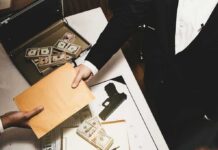 Ambassador Ousted After $100,000 Firestorm Two people exchange a manila envelope over a table with cash and a handgun