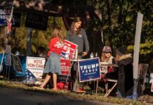 Poll Shock: Dems Surge, Power Still Slippery People at a campaign booth with political signs outdoors