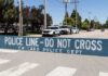 Police line barrier blocking a street with patrol vehicles behind