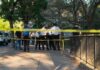 Serial Killer Fears Surge On River Trail Police officers gather behind yellow tape on a tree-lined sidewalk