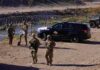 8,000 Troops, Fewer Crossings – Coincidence? Soldiers stand near barbed wire beside a police SUV