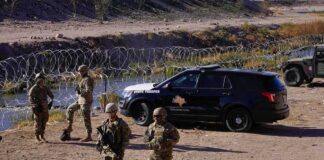 Soldiers stand near barbed wire beside a police SUV